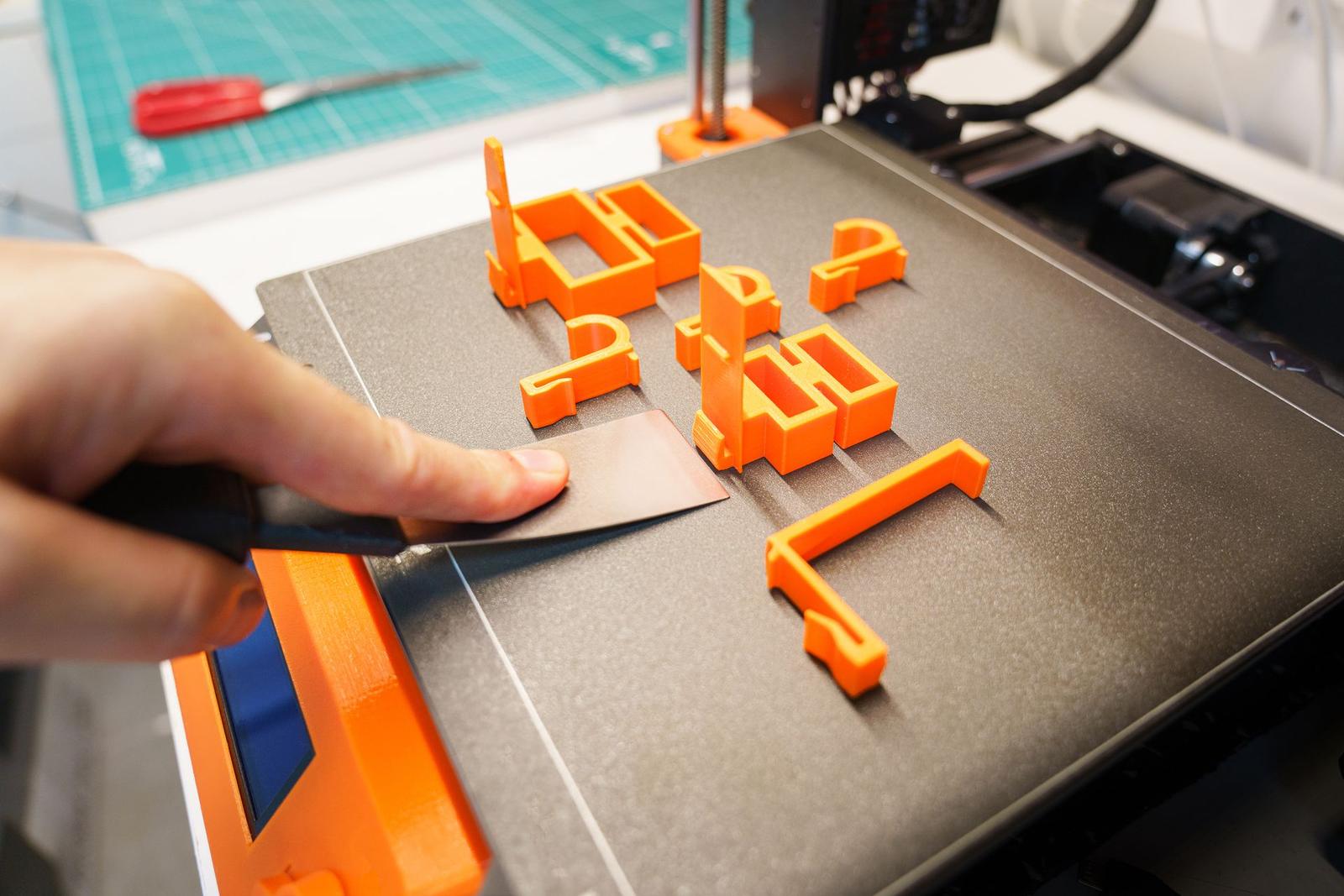 A maker smiling while holding a freshly 3D printed model next to a desktop 3D printer in a home workshop